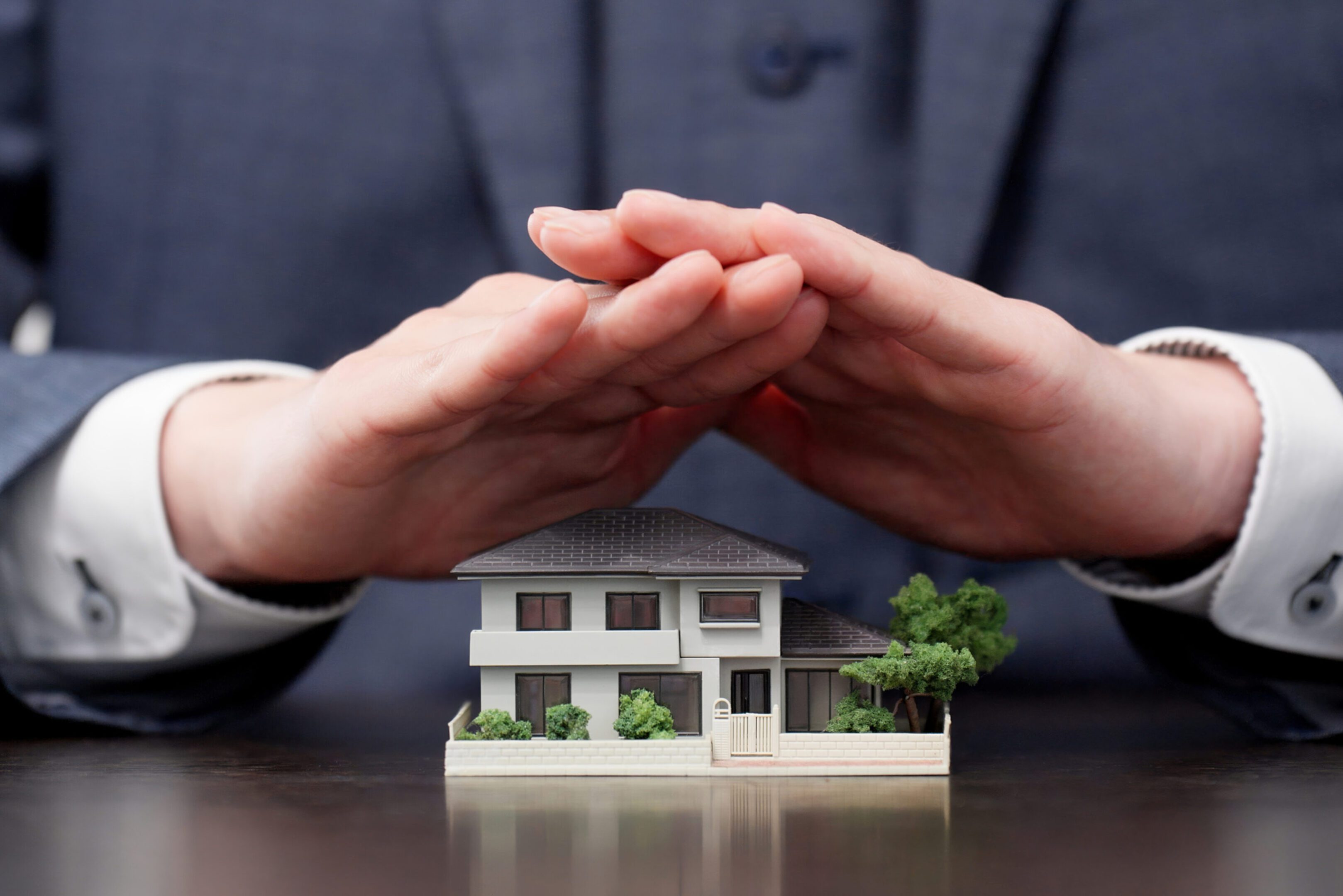 Hands protecting a miniature house model.